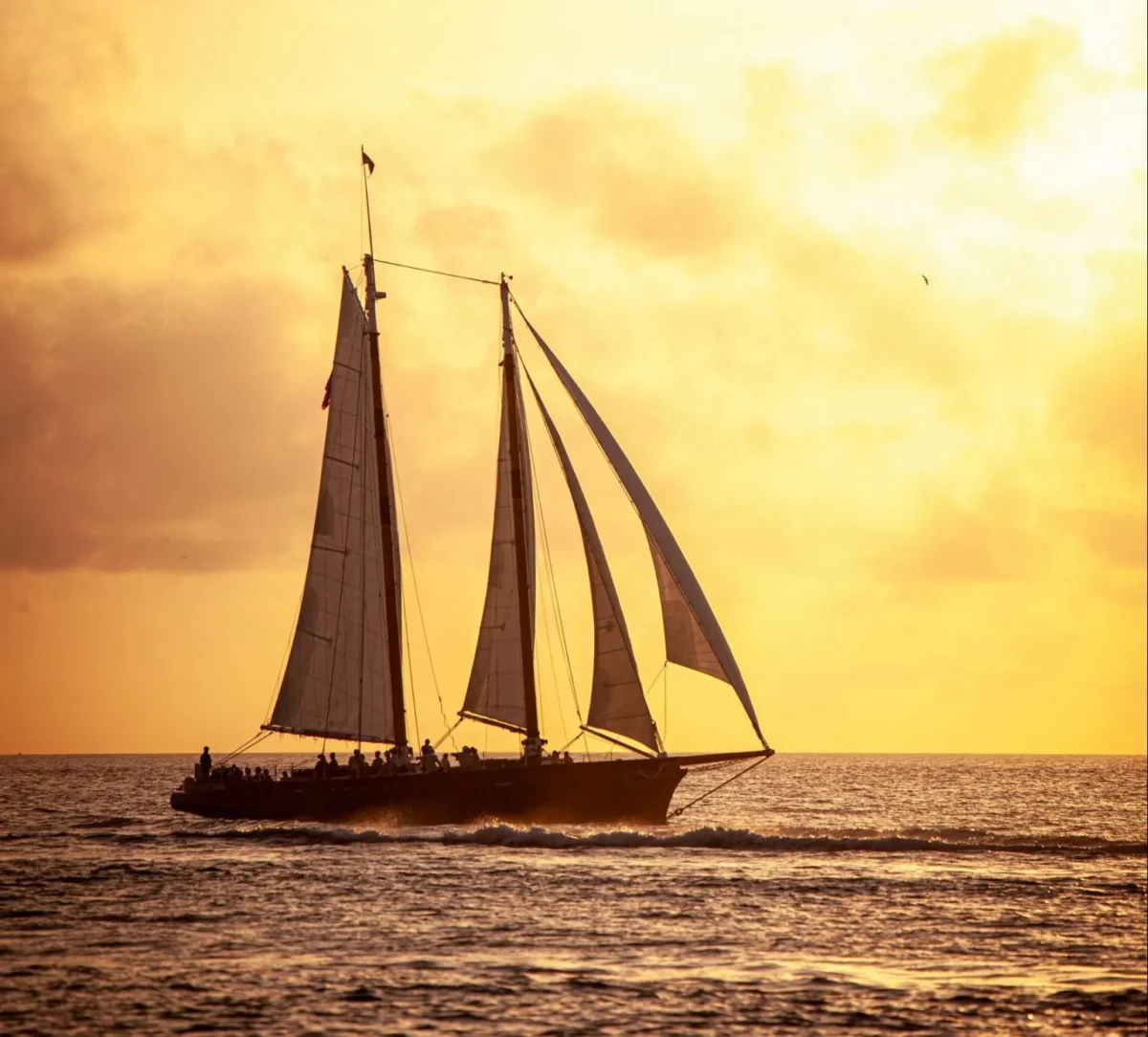 Traditional two-masted sailing boat under sail at sunset with passengers on deck